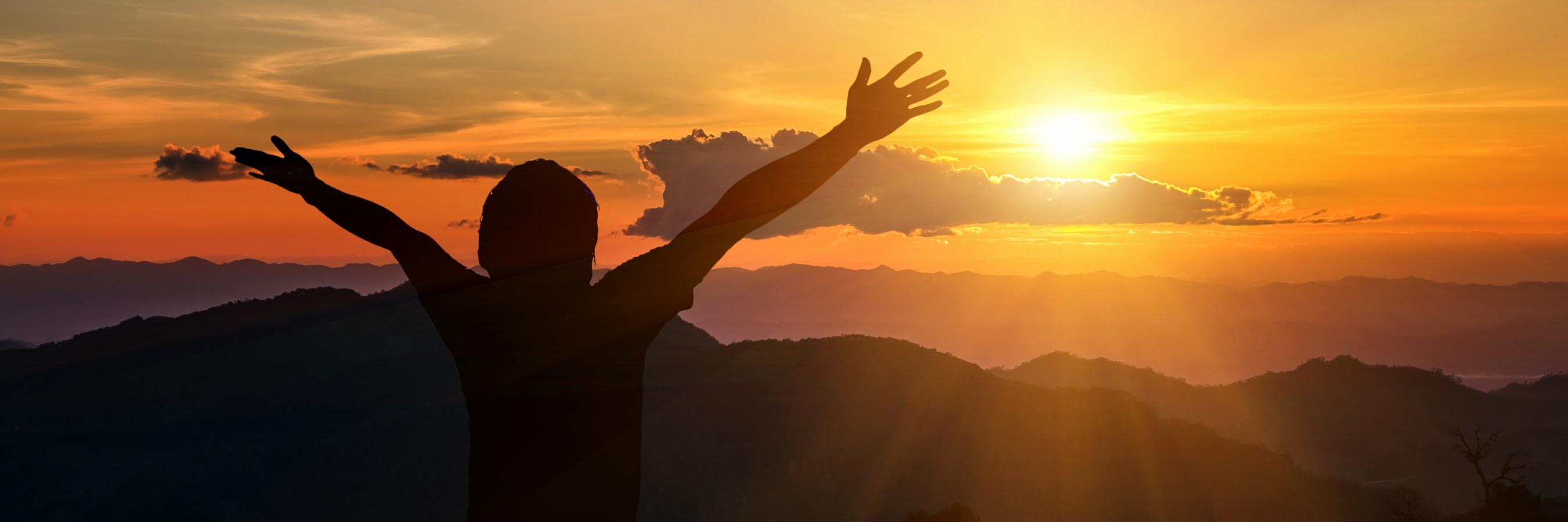 Person raises arms mountain sunset