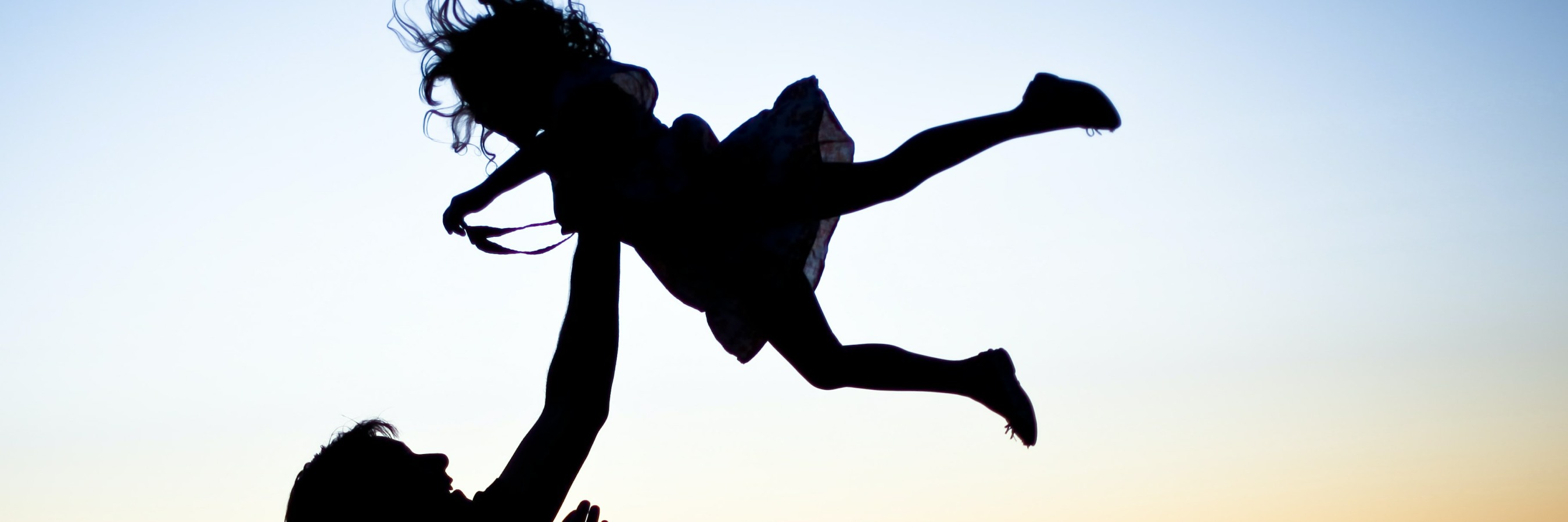 Parent catches child in air in silhouette