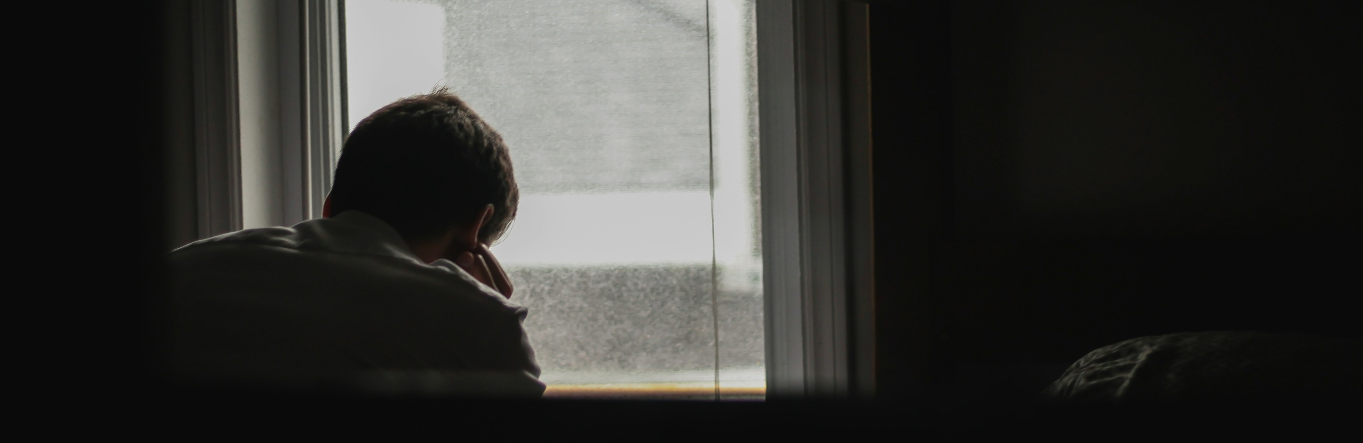 Man with bowed head looking out of a dark room